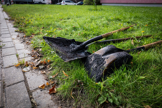 Asphalt-Covered Shovels Rest on Grass Beside a Paved Sidewalk