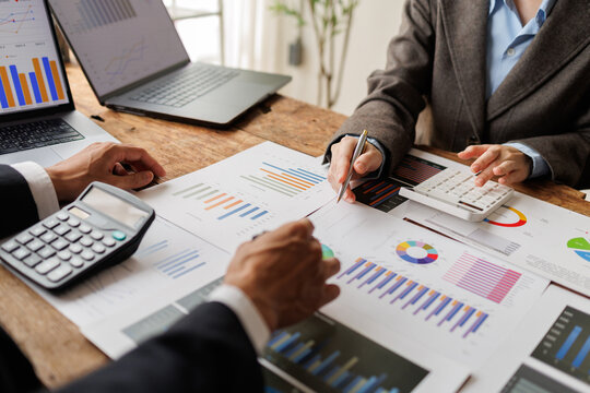 Financial professionals collaborating, analyzing business growth charts, calculating market data, and reviewing investment reports on a wooden office desk with a laptop and calculator