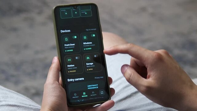 Person monitors smart home security devices on a smartphone, reflecting rising demand for connected protection, remote access control and real-time residential safety.