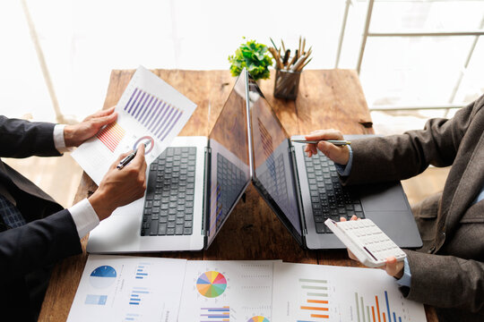 Business team collaborating over laptops, charts and reports, analyzing financial data and calculations to plan strategy, forecast growth and drive corporate success