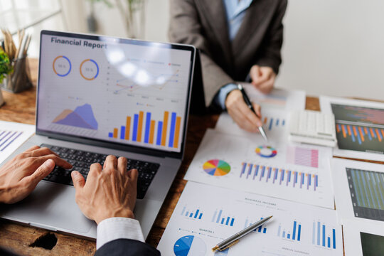Business professionals analyzing financial report data on laptop and paper charts. Collaborating on market analysis and economic strategy in a corporate meeting setting