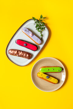 Assorted French eclairs with chocolate, berry and mint icing on plates. Elegant sweet food background, top view