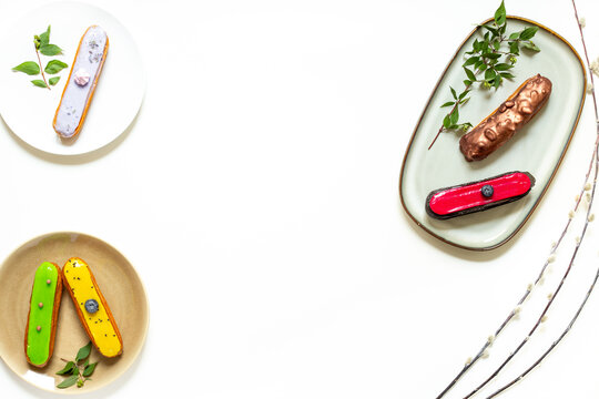 Assorted French eclairs with chocolate, berry and mint icing on plates. Elegant sweet food background, top view