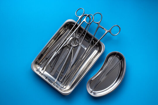 Sterile surgical instruments and tools - scalpels, scissors and others - in a stainless tray on blue background, top view