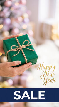 Woman's hands hold a green gift, with blurred festive lights symbolizing New Year celebration and sale.