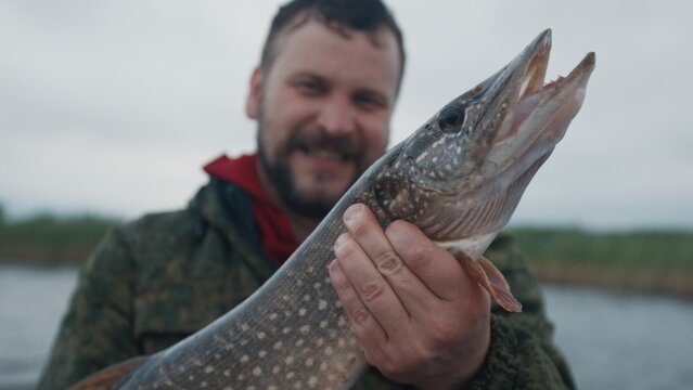 Fisherman sits in the boat on the lake and holds the trophy pike fish