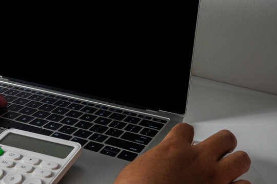 Close up of hands typing on a laptop with a blank black screen and using a calculator. Concept of accounting, financial planning, calculating budget, late night work, and data entry.