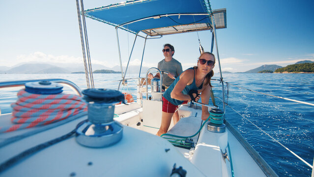 Sailing in the smooth sea during sunny day, woman works with the ropes. Man and woman sail the small sailing boat in the region of the island of Ilha Grande in Brazil