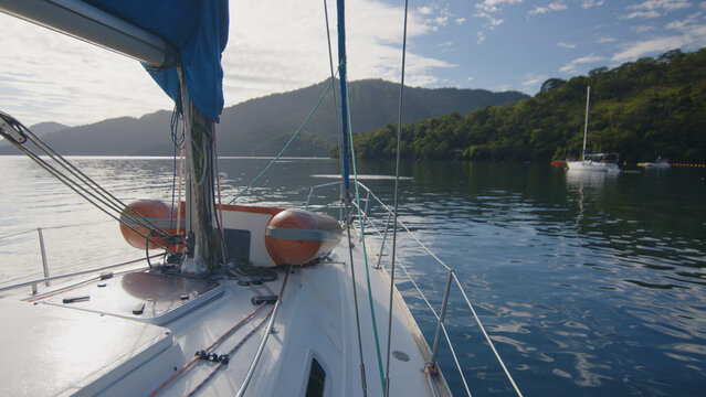 Sailing boat anchored in the calm bay at sunrise, view from the deck to the bow