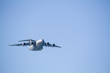 Fototapeta premium C-17 Globemaster III military transport aircraft in flight, viewed from below against a blue sky with a white cloud below the aircraft, showing its four jet engines and distinctive high-wing design.