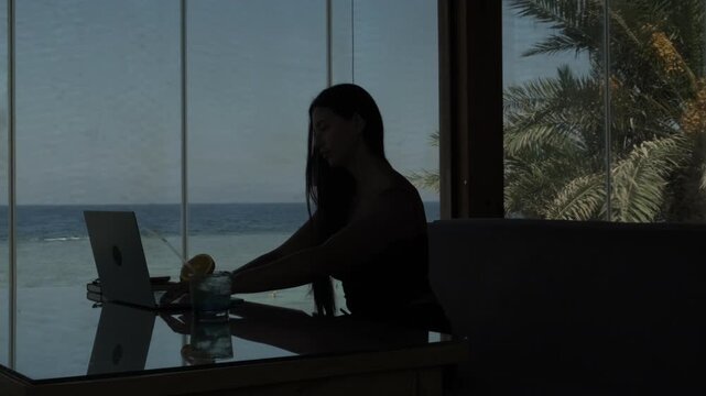 Woman working on laptop by the sea, symbolizing work life imbalance and inability to disconnect in beautiful surroundings