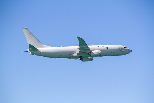 P-8 Poseidon maritime patrol aircraft flying in side profile against a clear blue sky, showing its swept wings, twin jet engines, fuselage and distinctive aircraft design.