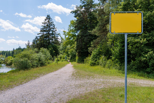 Blank yellow sign post mock up next to gravel path in green nature, customized text and direction decision concept