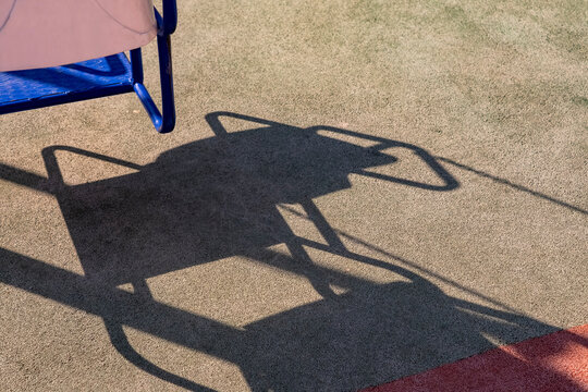 Swing shadow on playground surface. Artistic representation of play and shadow. Golden hour lighting creates high contrast and a nostalgic, quiet atmosphere.