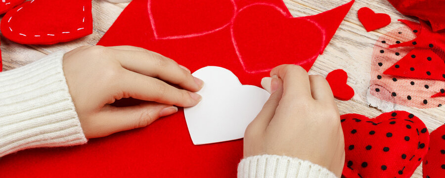 women's hands make red hearts from the fabric. Preparation for St. Valentine's Day. homemade festive decorations. Above view, flat lay