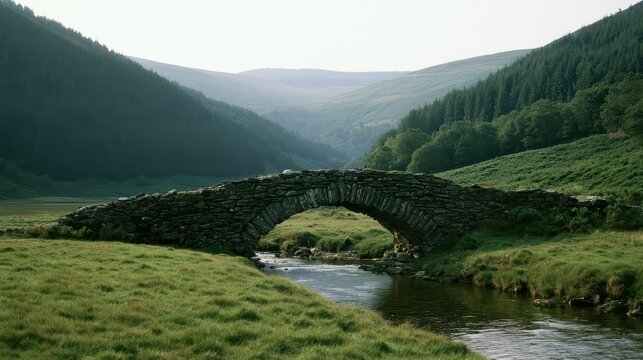 An ancient stone packhorse bridge spanning a gentle river in a lush green valley. Atmospheric landscape photography ideal for travel and historical concepts.