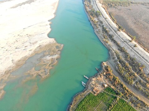 Aerial view of the Indus River with small boats moored along the sandy banks near agricultural fields in Dera Ghazi Khan, Punjab, Pakistan.