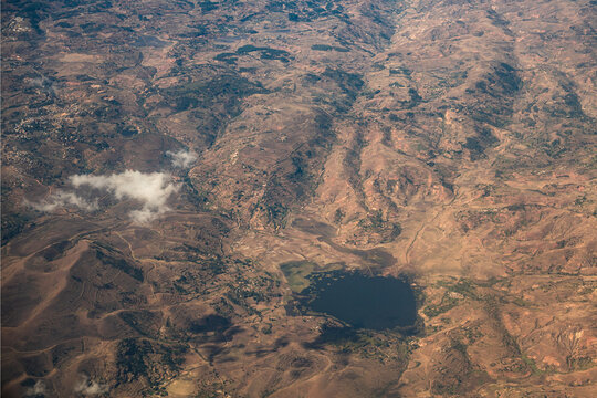 Aerial view of the rugged landscape featuring rolling hills, dry terrain, and a small dark lake visible from a flight between Morondava and Antananarivo. Madagascar.