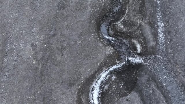 Aerial view of a stream running down a large glacier covered in black ash in the central highland of Iceland