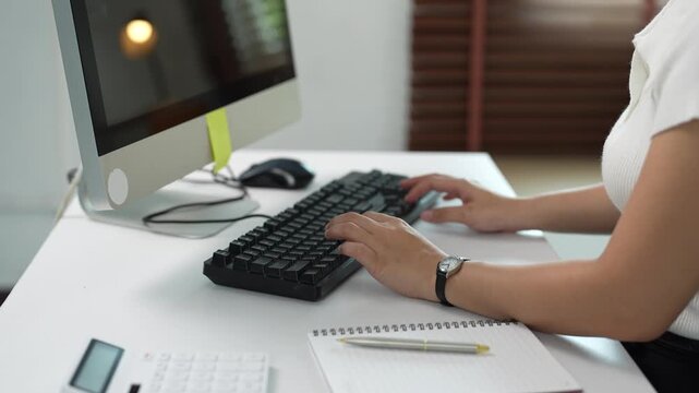 Businesswoman typing on a keyboard at her desk while working on a computer in a modern office, showing the concept of data entry, programming, and online communication
