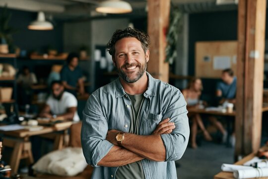 Middle aged man with a beard smiling with arms crossed in a modern open plan office workspace