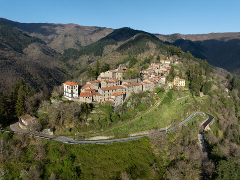 Aerial view of the historic village of Chiassaia perched on a hillside, featuring stone houses with terracotta roofs, surrounded by lush green slopes and winding roads in Chiassaia, Tuscany, Italy.