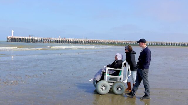 Supportive Friends and Family Walking with a Person in an Accessible All-Terrain Wheelchair on a Sunny Beach