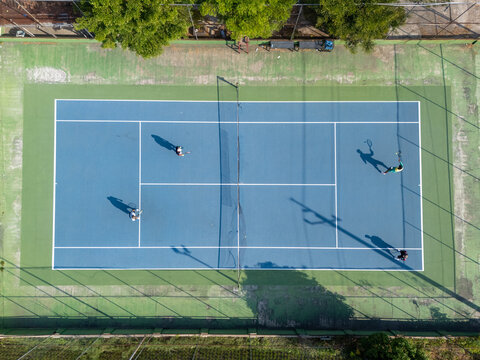 Aerial view of four people playing tennis on a blue court surrounded by green borders in Klaten, Central Java, Indonesia.