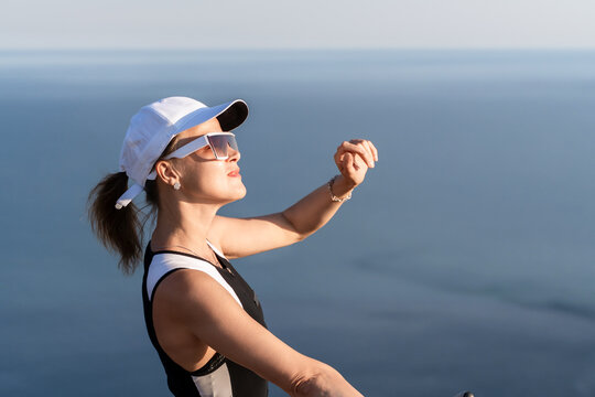 Woman hat sunglasses standing outdoors by the ocean looking at her watch on a sunny summer day with copy space