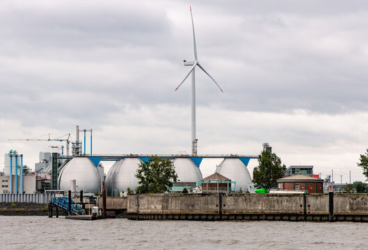 Modern industrial wastewater treatment plant with egg shaped digestion tanks and wind turbine on riverbank, green energy and environmental engineering concept