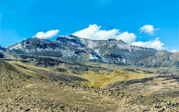 A view of rugged, high altitude landscape with a prominent snow-capped peak in the Andes Mountains in southern Peru in the dry season