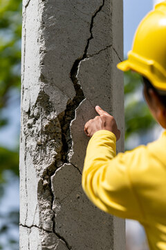 A person wearing a safety helmet and shirt examining a structural failure in a concrete wall.