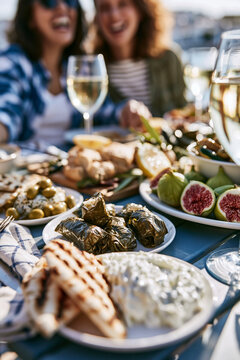 A sunny patio table at a seaside cafe in Greece or Italy, featuring small sharing plates: grape leaves, grilled pita , tzatziki, fresh figs, and wine.