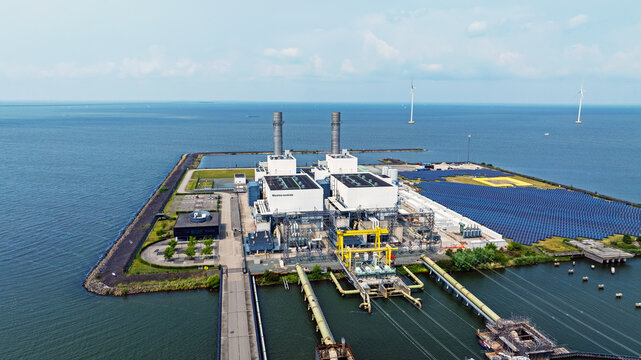 Aerial view of the Flevocentrale power plant on a peninsula in the IJsselmeer, featuring industrial buildings, solar panels, and wind turbines in Lelystad, Flevoland, Netherlands.
