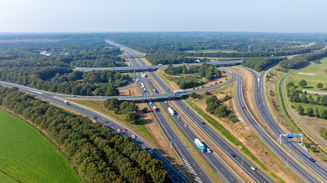 Aerial view of a highway interchange with multiple lanes, vehicles, and surrounding green forests and fields in Eemnes Utrecht, Netherlands.