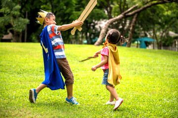 Naklejka premium Two children playfully sword fighting in a park, wearing capes.
