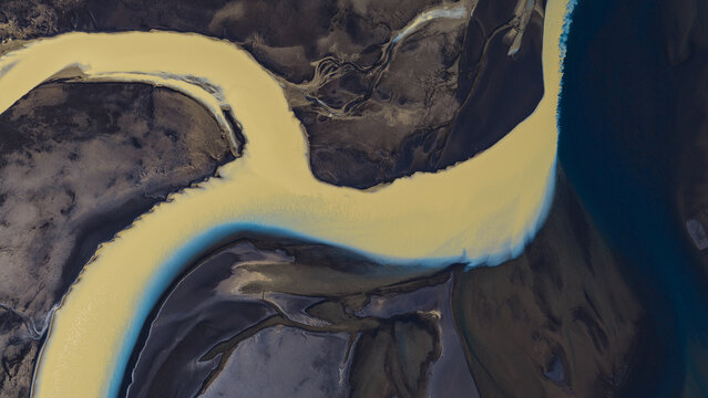 Aerial view of the winding Tungnaa river featuring vibrant yellow glacial silt contrasting with dark volcanic terrain in Skaftarhreppur, Iceland.