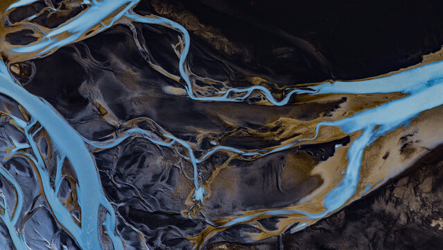 Aerial view of the braided Tungnaa river with vibrant glacial blue water flowing through dark volcanic sand deposits in Skaftarhreppur, Iceland.