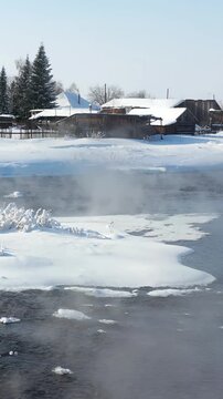 Vertical video view from low-altitude flying drone on russian Altai country village Semiletka. Not freezing river Koksha in winter season. The banks are covered with snow. Altai Krai.
