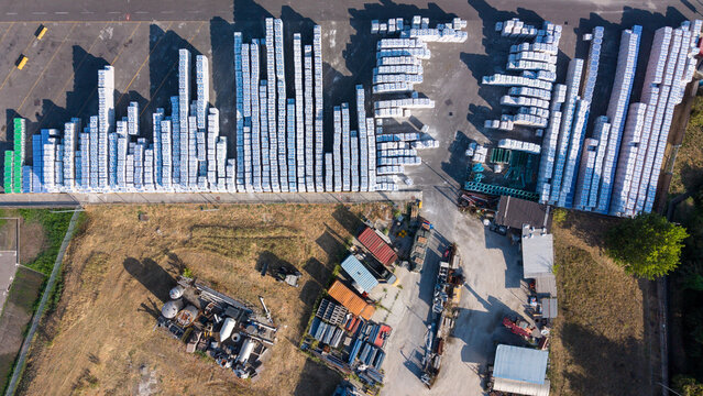 Aerial view of a construction materials manufacturing facility with rows of stacked white bags, industrial storage areas, and processing infrastructure in Milan, Lombardy, Italy.