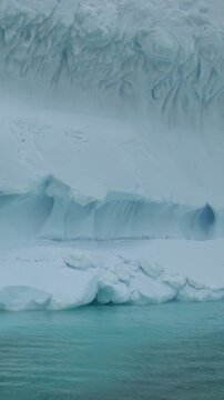 Giant icebergs tower above the tranquil sea, reflecting the soft hues of the Antarctic sky. The stillness surrounds the icy giants as they slowly shift and reshape in the cool air.