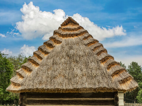 Traditional Thatched Roof Cottage With Layered Straw Thatch Against Blue Sky