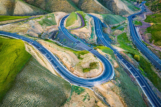 High angle view of winding asphalt road curving through green mountain hills, creating intricate transportation pattern.