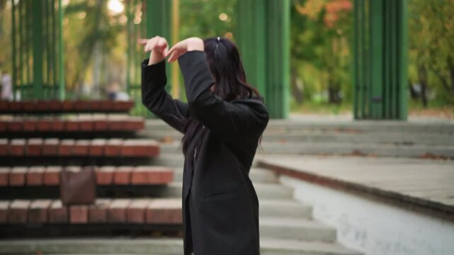 Close up of woman performing graceful dance movements in outdoor park setting with green metal structures and brick steps. Woman maintains fluid motion throughout demonstrating expressive