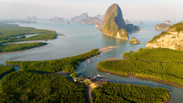 Aerial view of Phang Nga Bay with limestone karsts rising from the water, surrounded by lush mangrove forests and small boats moored in the bay, Thailand.