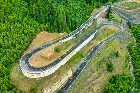High angle view of a winding serpentine mountain highway passing through dense pine forest.