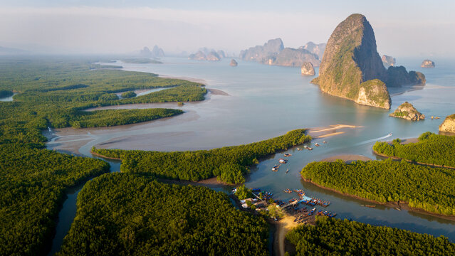 Aerial view of Phang Nga Bay featuring lush mangrove forests, dramatic limestone karst formations, and small boats moored in the calm waters of Thailand.
