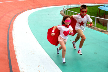 Two children in superhero costumes running on a colorful track. © Rawpixel.com