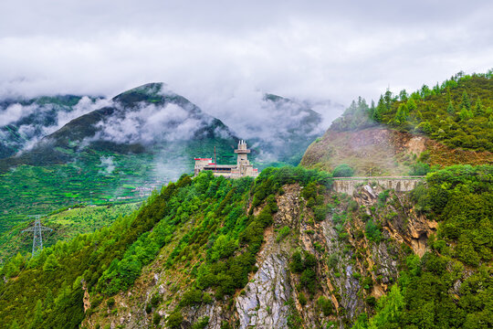 Scenic view of lush green mountain ridge and modern observation building shrouded in fog and clouds in Sichuan, China.