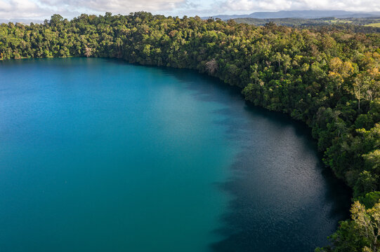 Aerial view of the deep blue waters of Lake Eacham surrounded by dense tropical rainforest in the crater of an extinct volcano in Atherton Tablelands, Queensland, Australia.